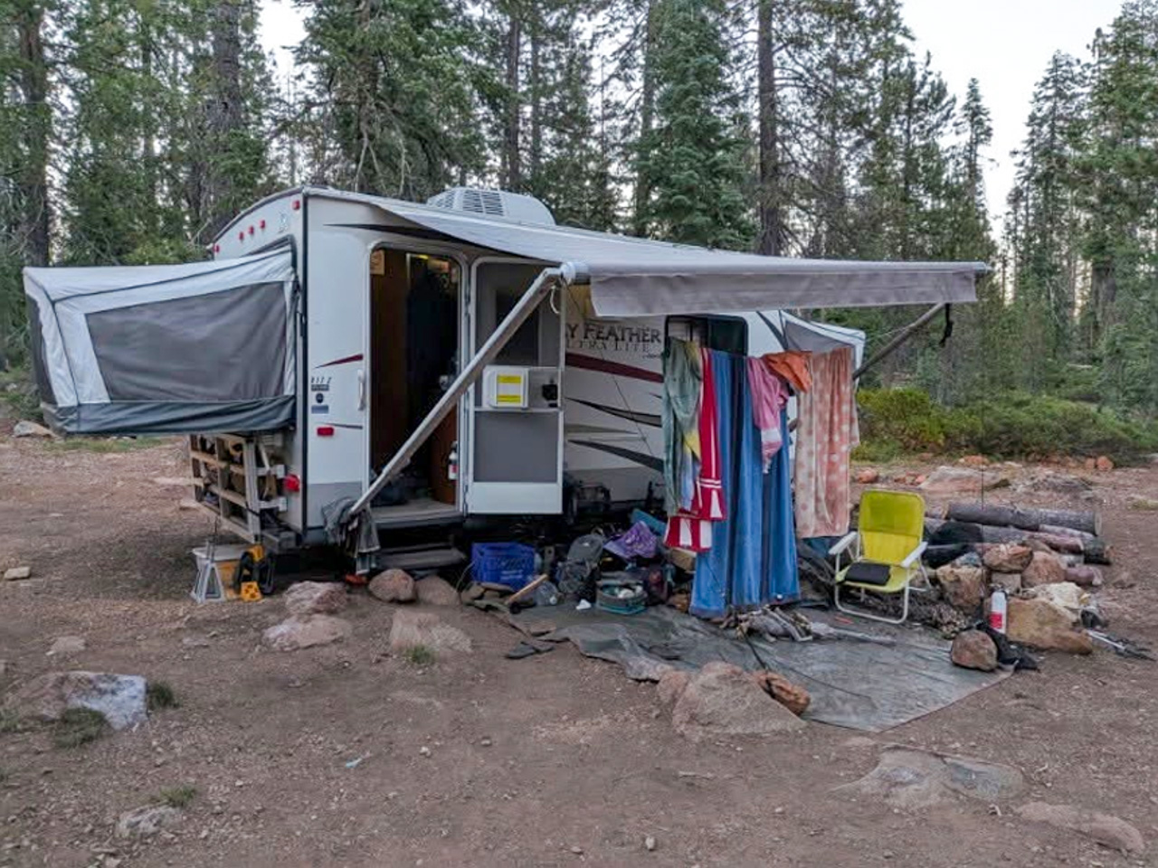 Camper trailer set up in a forest clearing with a clothesline and outdoor seating area under an awning.