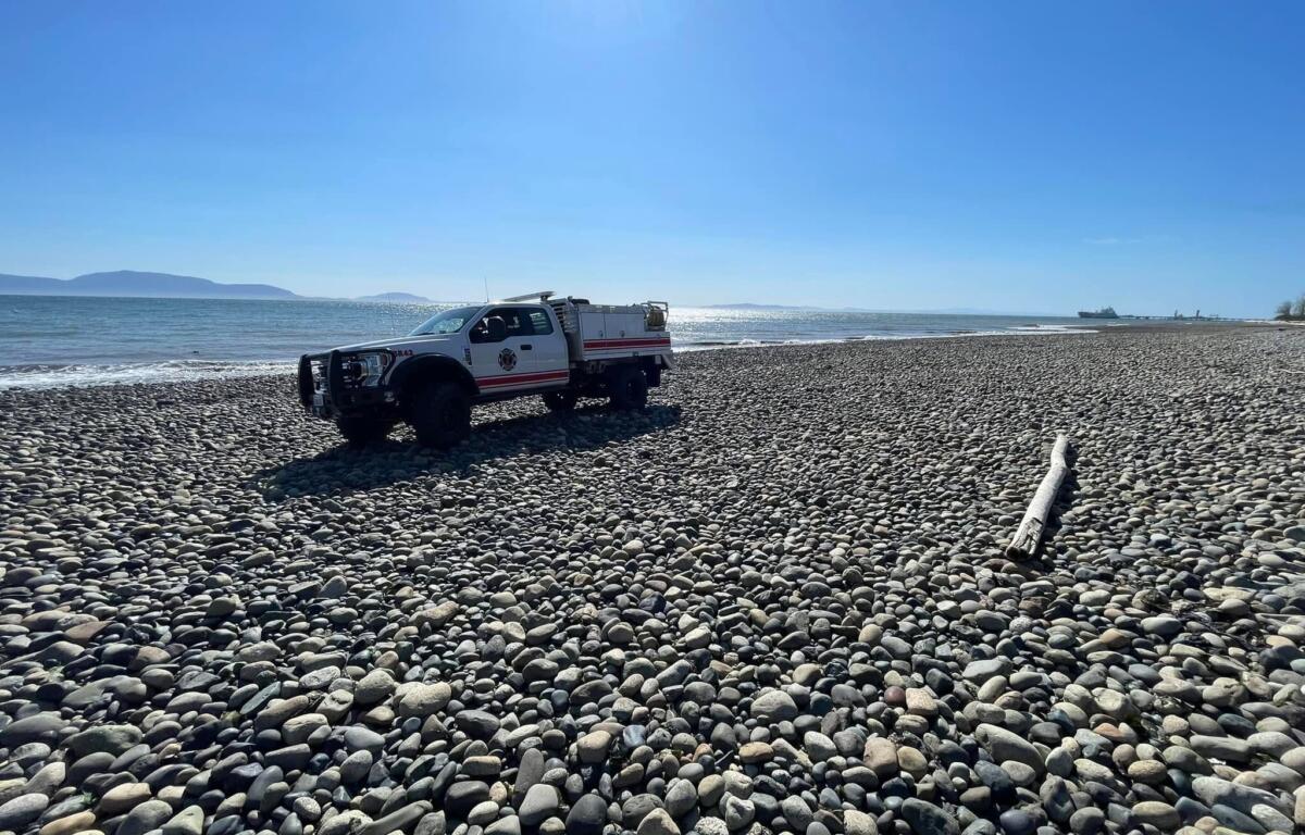 White rescue truck parked on a pebble beach with the calm sea and clear blue sky above.
