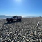 White rescue truck parked on a pebble beach with the calm sea and clear blue sky above.
