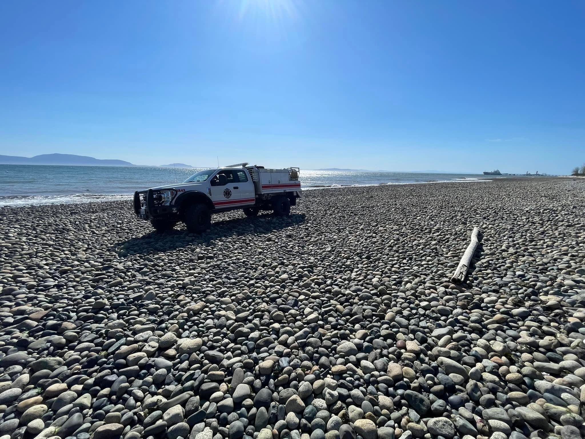 White rescue truck parked on a pebble beach with the calm sea and clear blue sky above.