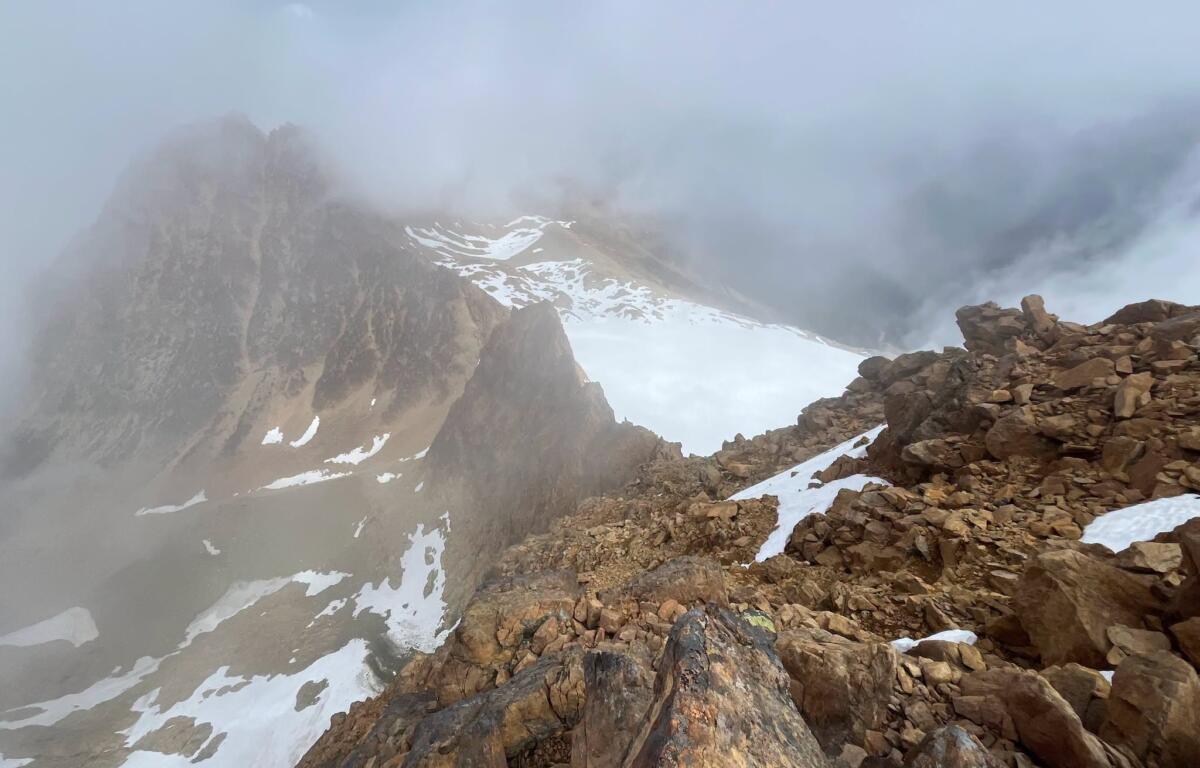 Snowy, jagged mountain ridge veiled in thick fog and pale blue sky above.