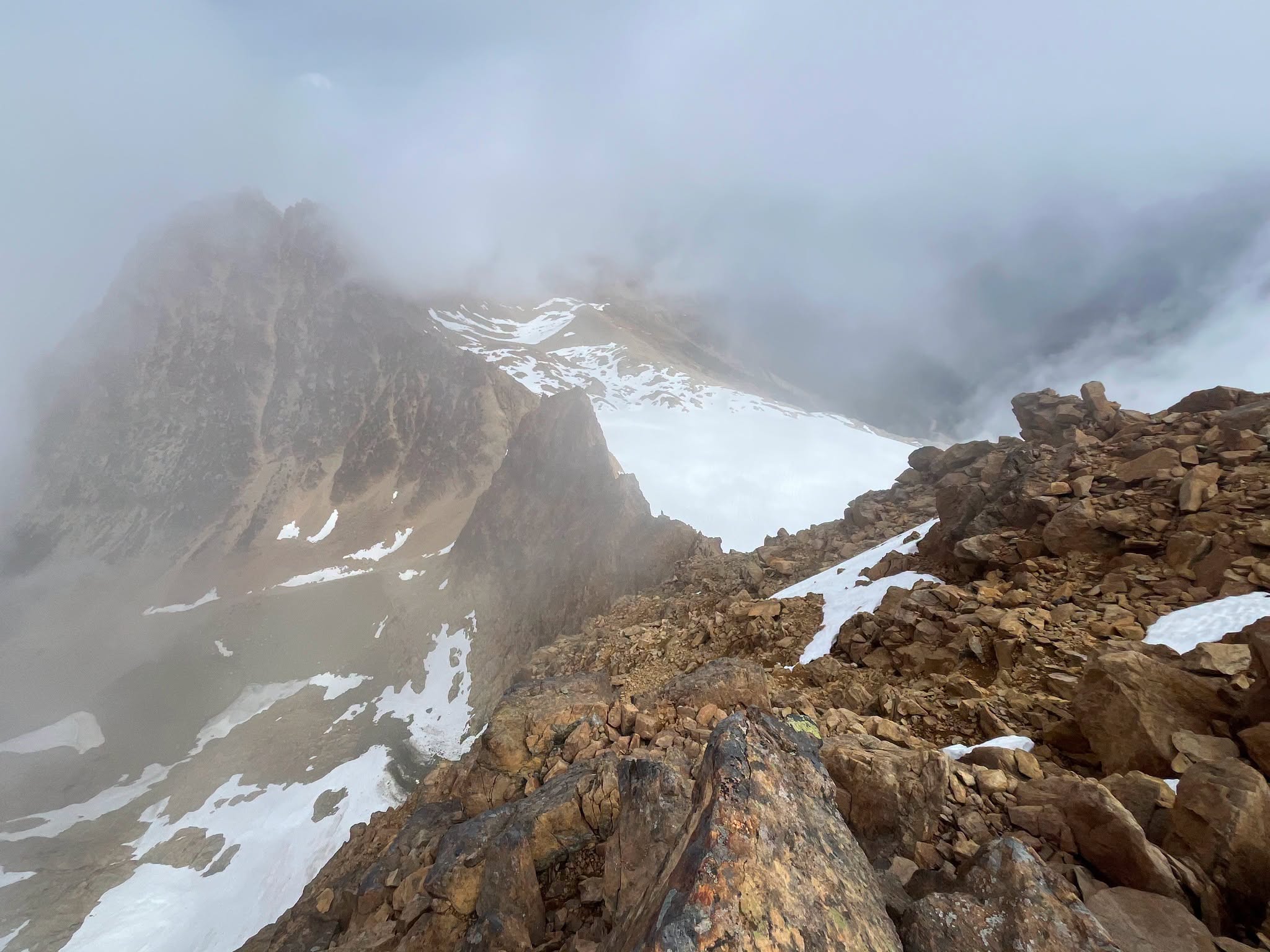 Snowy, jagged mountain ridge veiled in thick fog and pale blue sky above.